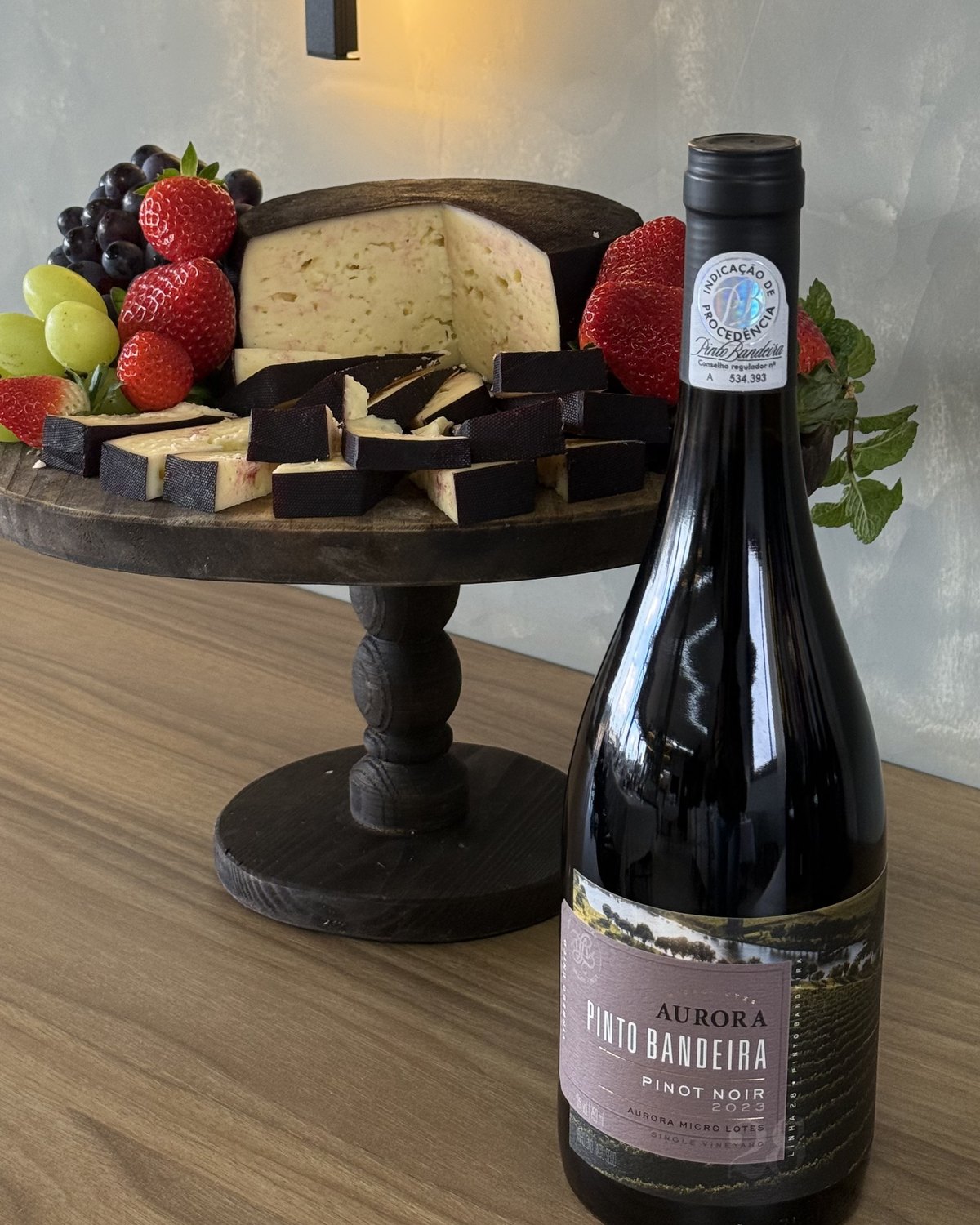 Garrafa Aurora Pinto Bandeira Pinot Noir ao lado de tábua de queijos e frutas